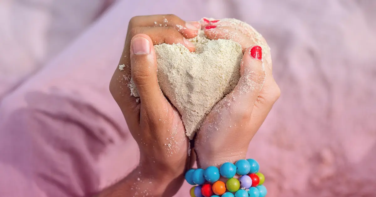 Hands holding heart-shaped sand at beach.