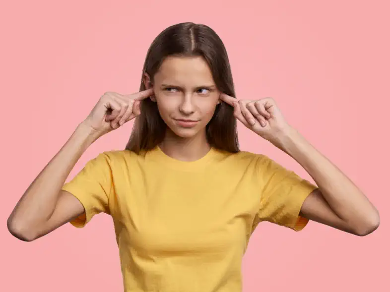 Woman blocking ears with fingers, pink background.