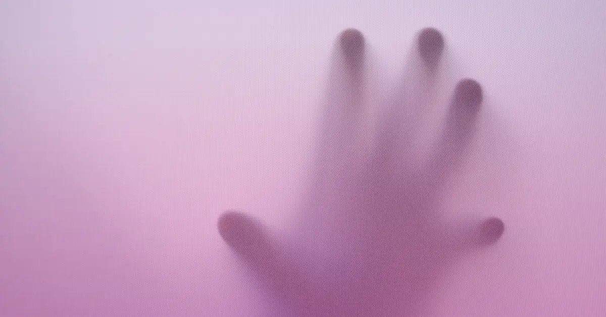 Blurred hand on frosted pink glass surface.