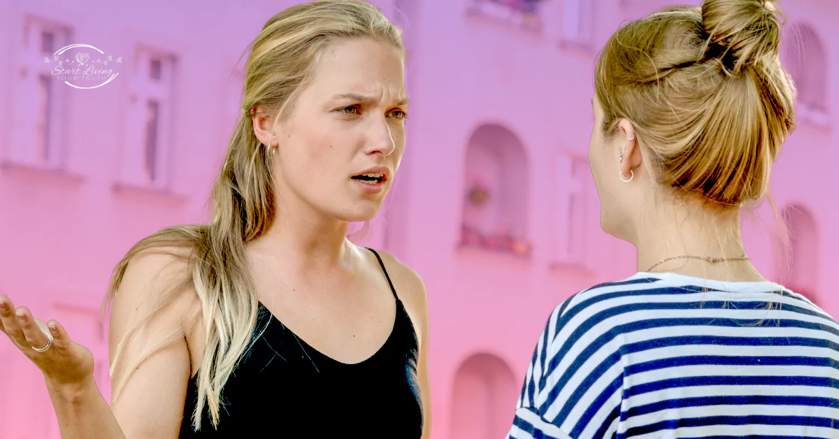 Two women talking, one looks concerned, pink building background.