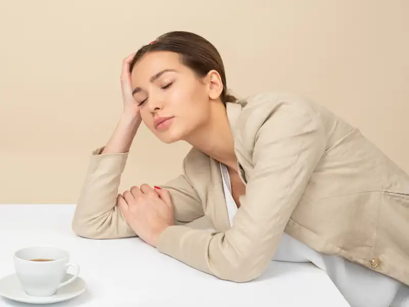 Tired woman resting head on hand, coffee nearby.