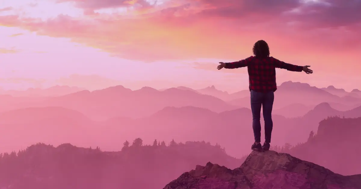 Person on mountain at sunset, arms outstretched.