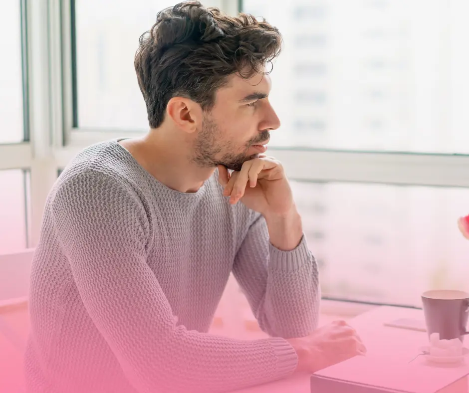 Man pondering, sitting indoors with coffee cup.